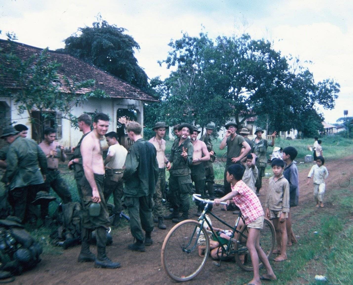 Group of U.S. soldiers in a Vietnamese village, children standing nearby.