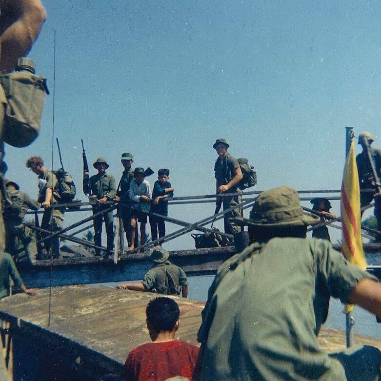 Soldiers and civilians standing on a bridge.