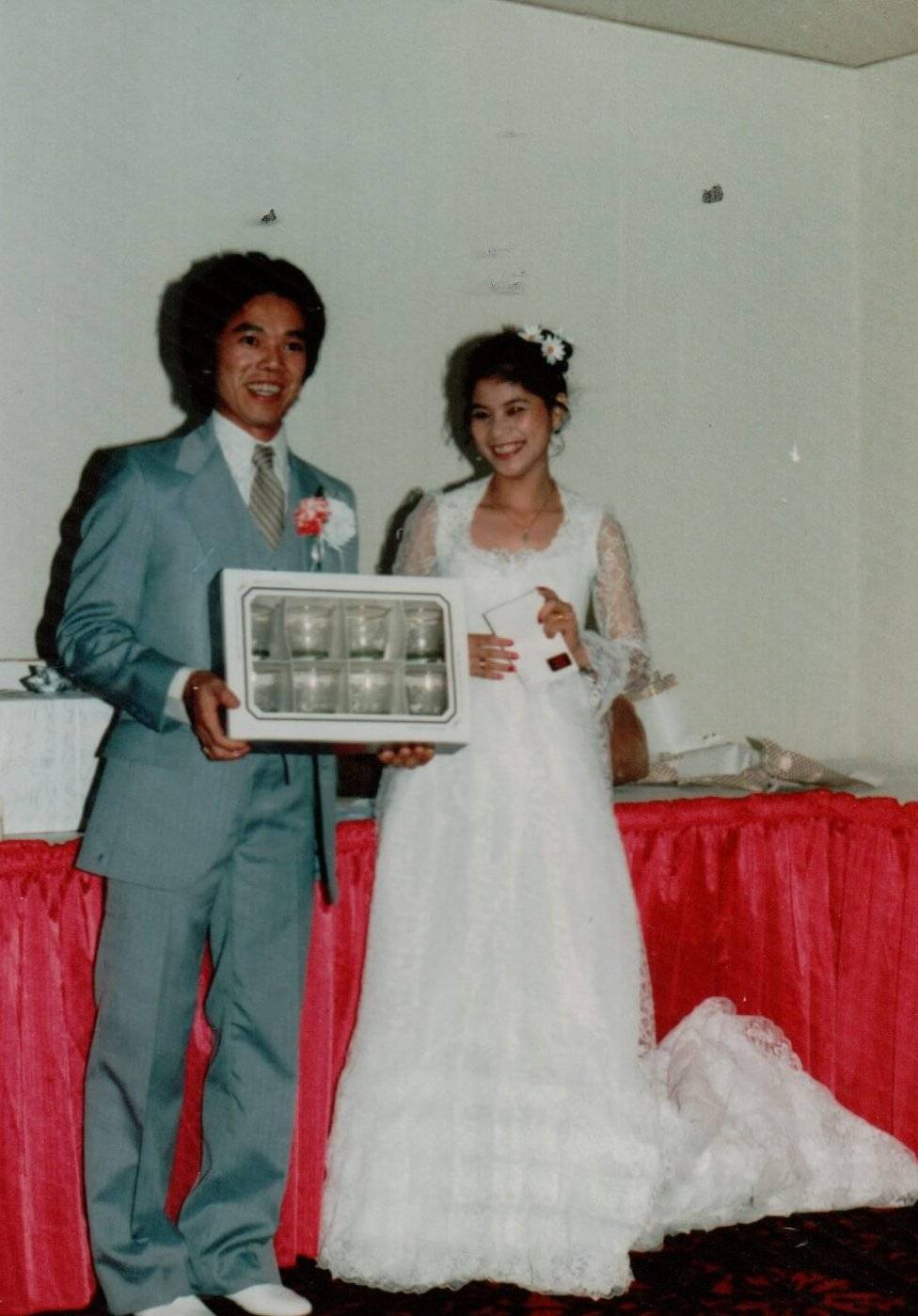 An Asian bride and groom holding up a gifted set of glasses.