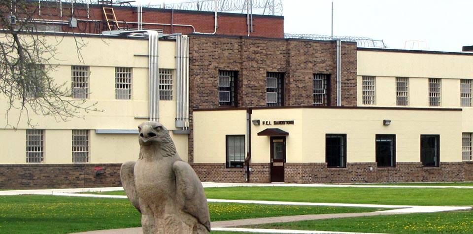 An exterior shot of a low-security prison, an eagle statue in the foreground.