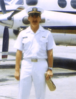Man in white Navy uniform, holding a bottle in a brown paper bag.