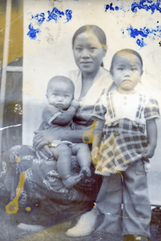 Portrait of a Hmong mother with two young children, image distorted by ink smudges.