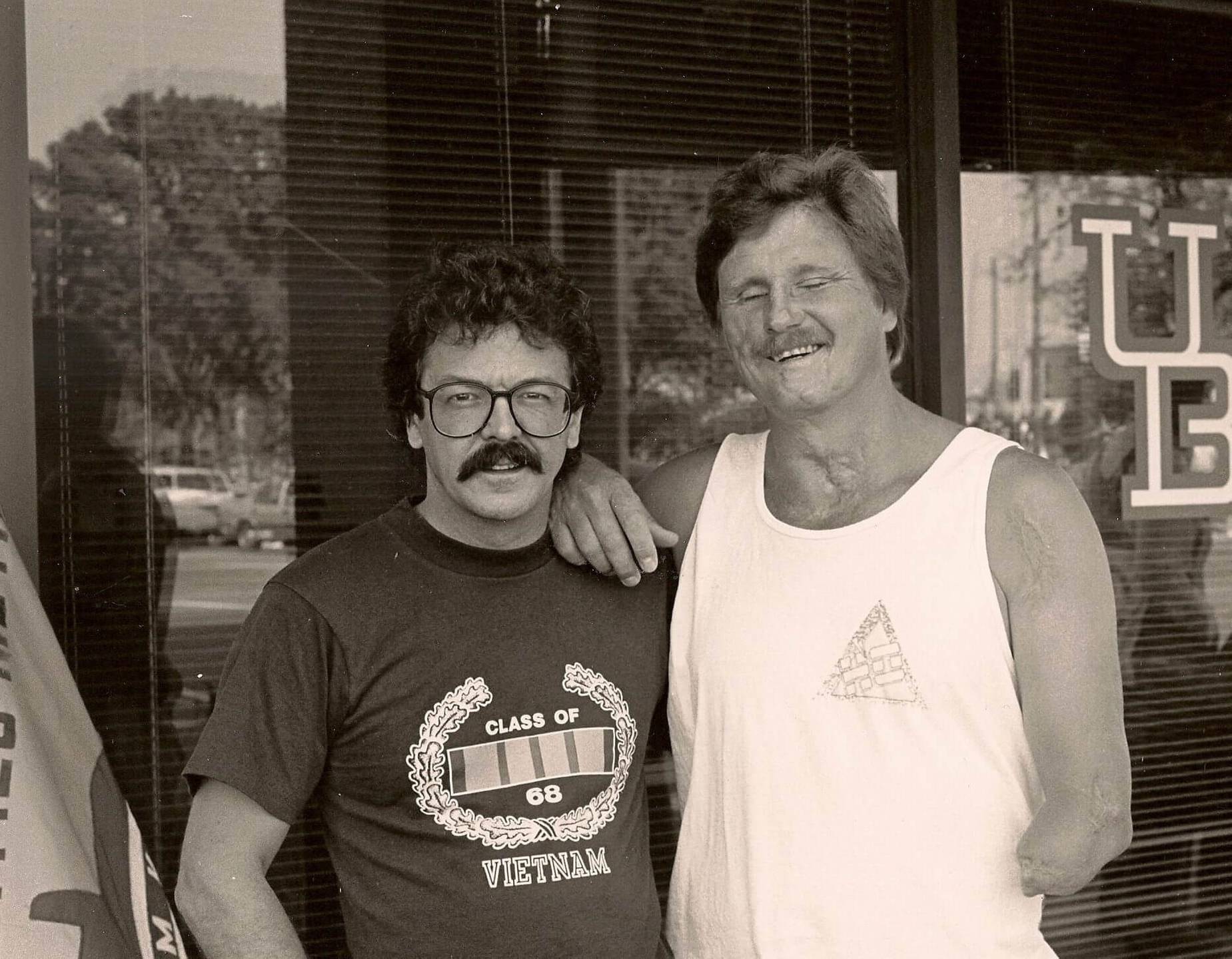 Picture of two U.S. vets. One wears a "Class of 68 Vietnam" shirt, the other is missing an arm from the elbow down.