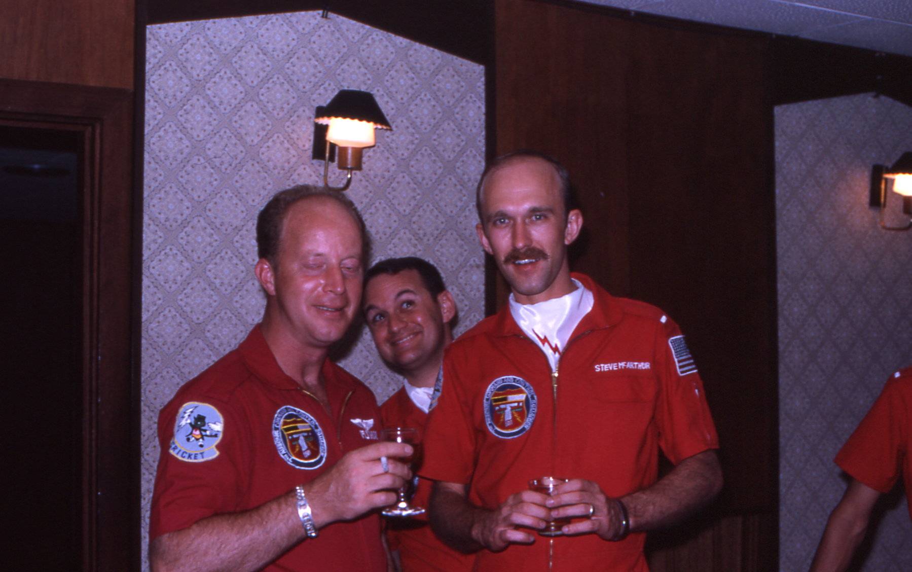 Three men in orange flight jumpsuits inside what looks to be a hotel.