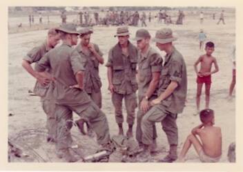 U.S. soldiers in fatigues, on a beach. Vietnamese children hang out nearby.