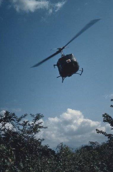 A helicopter with red cross on its nose, flying above some foliage.