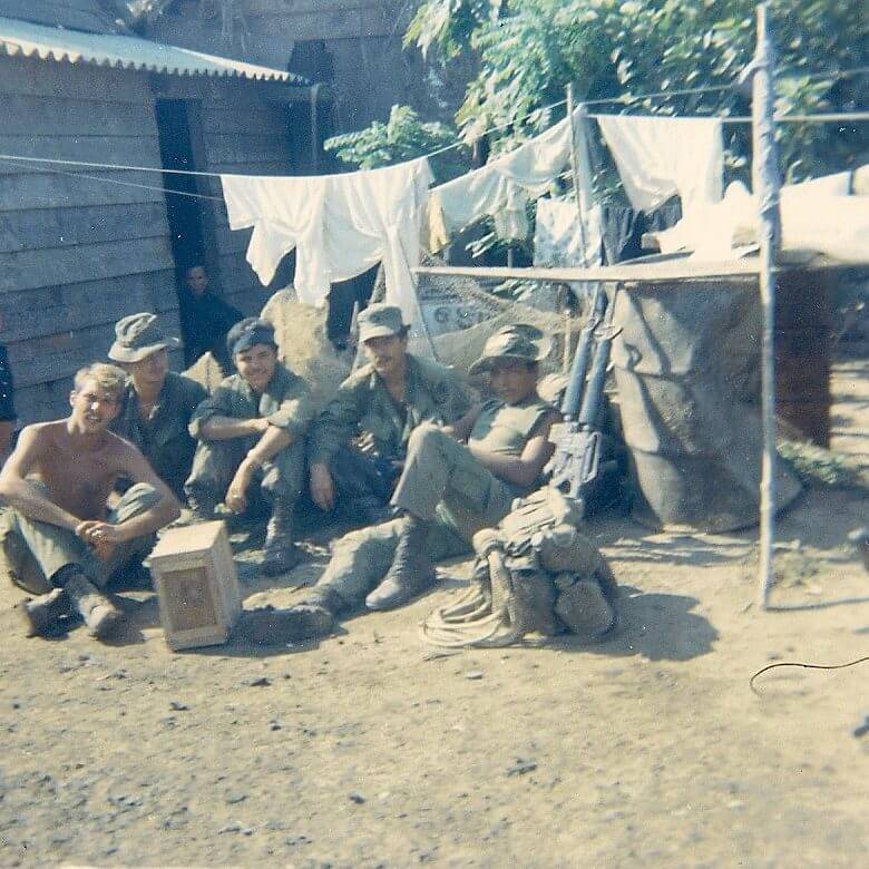 Soldiers hanging out outside in a Vietnamese village, clothes drying on a line in the background.
