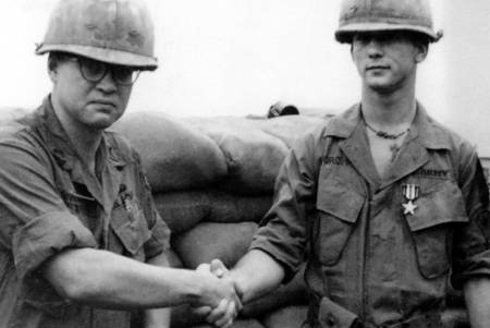 Two U.S. soldiers in helmets shaking hands and looking at the photographer.