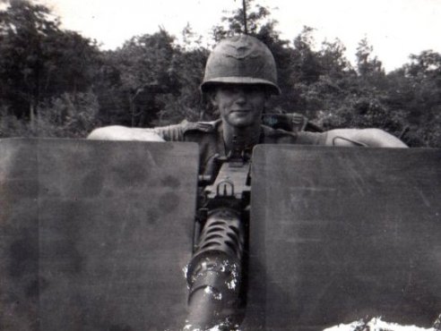 A young U.S. soldier posed behind a large, mounted gun.