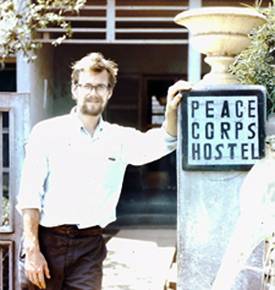 A young man leaning against a "Peace Corps Hostel" sign.