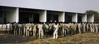 A large group of African children in white and khaki clothing, gathered outside a one-story school building.
