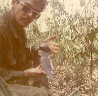 U.S. soldier wearing sunglasses, holding up a piece of shrapnel for the camera.