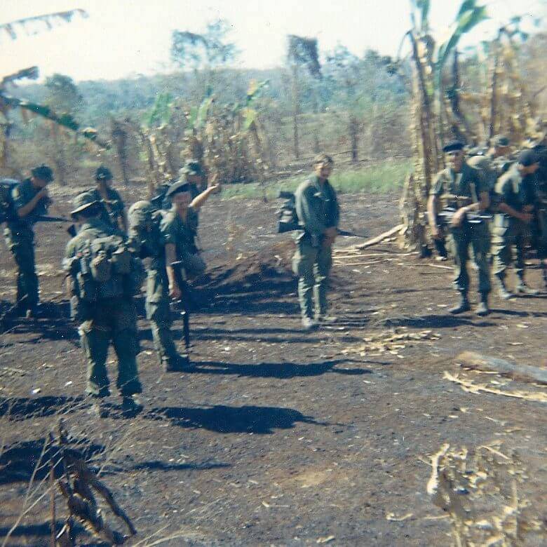 Soldiers standing in a muddy clearing.