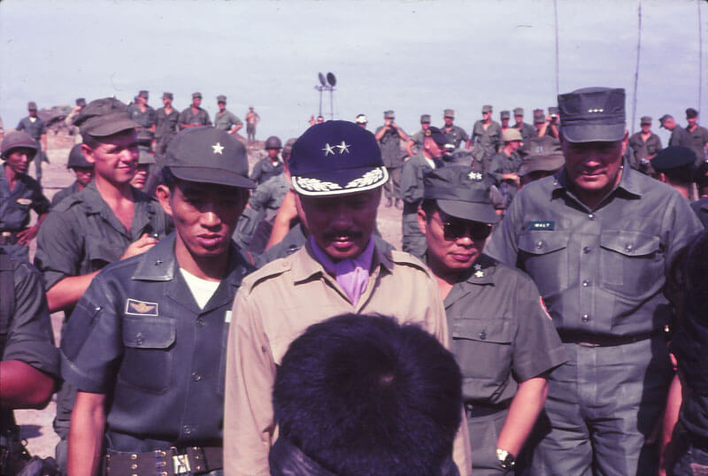 Stately Vietnamese figure, taken head on, over the head of a prisoner. Other Vietnamese soldiers stand behind the general.