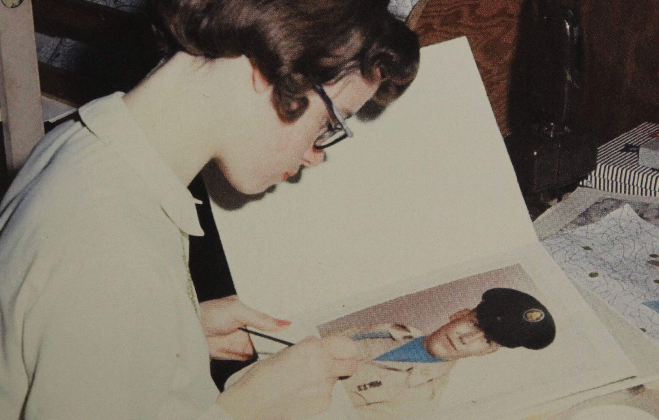 A young woman with paintbrush in hand, colorizing portraits of soldiers.