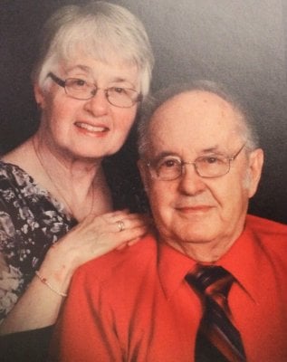 Contemporary portrait of an older couple, both wearing glasses.