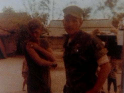 Blurry image of two soldiers, one examining his right bicep.