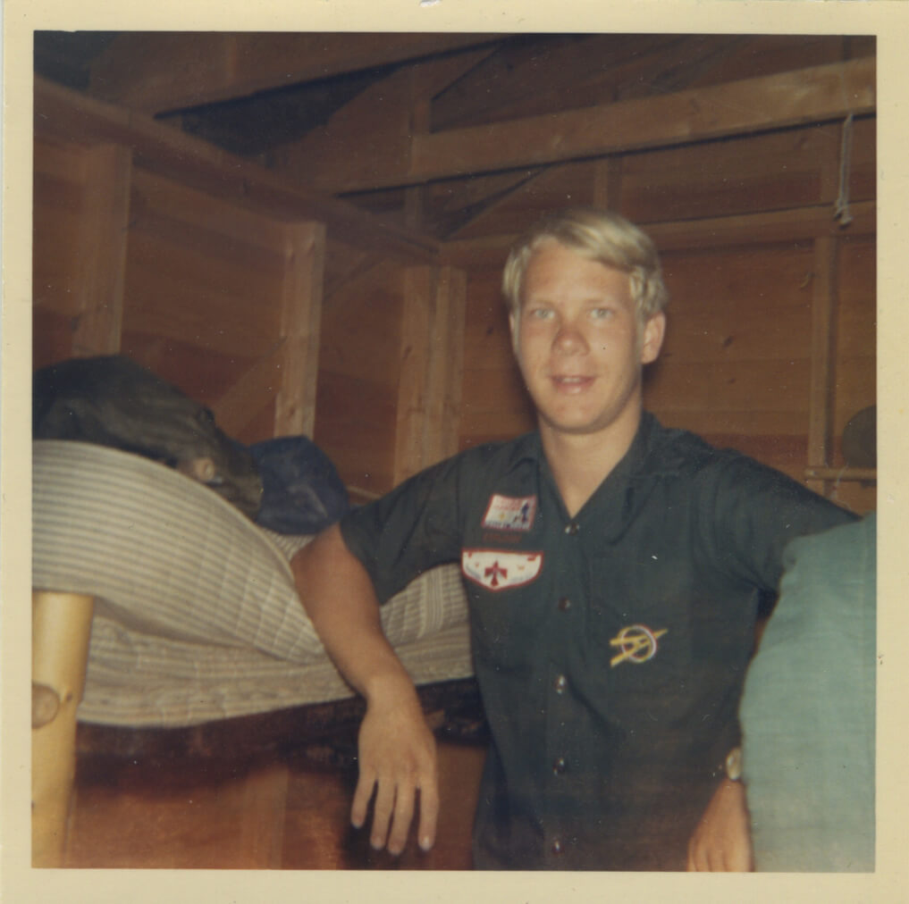 A young man standing by a bunk in his Eagle Scout uniform.