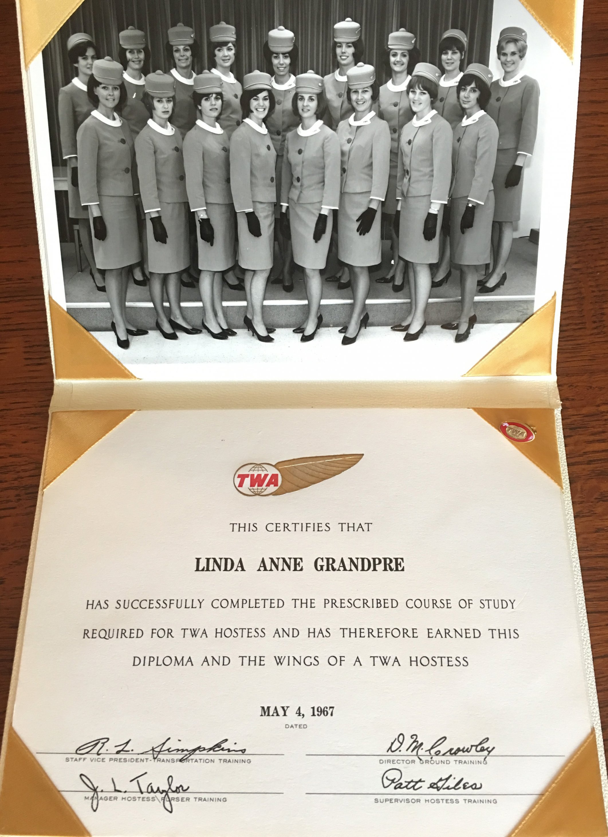 A mounted certificate for completing TWA flight attendant training and a photo of a group of about a dozen attendants in uniform.