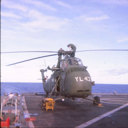 Helicopter with "YL-23" painted on the front sitting on the flight deck of ship (possibly USS Iwo Jima) with the ocean in the background.