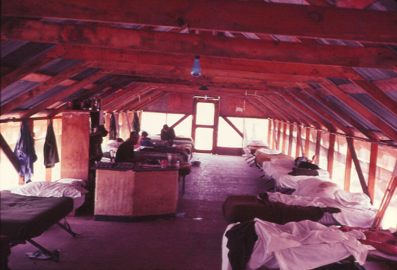 Wood frame building with cots setup, in center is a workstation for a nurse or hospital ward.