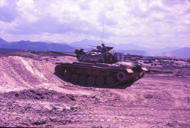 Tank driving towards the viewer's left up an embankment of dirt.