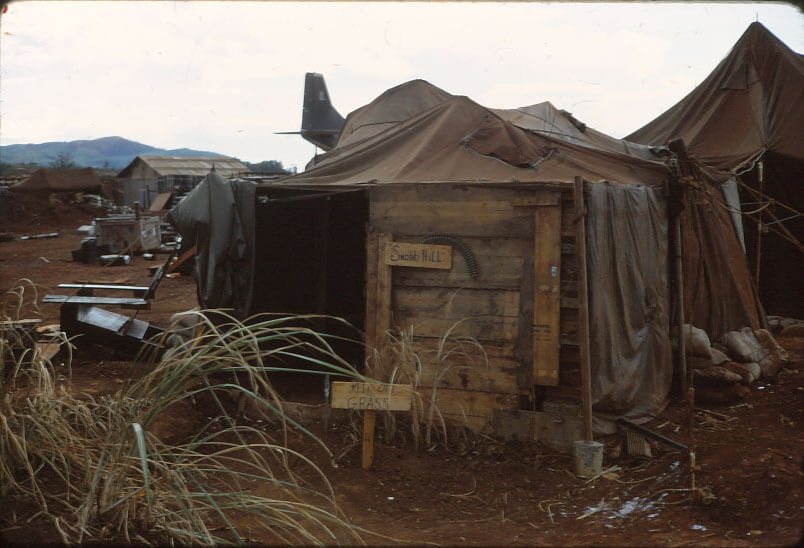Soldier's quarters consisting of wood and a canvas roof; grass to the left and a a sign that says "Keep off the grass".