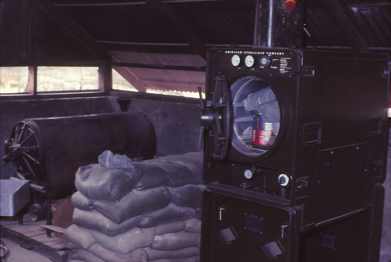 Two sterilizer machines with sandbags in between; wall panels are partially open to the outside.