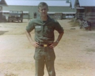 Young U.S. soldier standing outside a base, hands on hips.