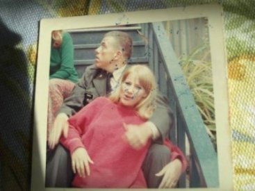 A young woman in a pink sweater lounging in the lap of a young soldier, who is looking over his shoulder.