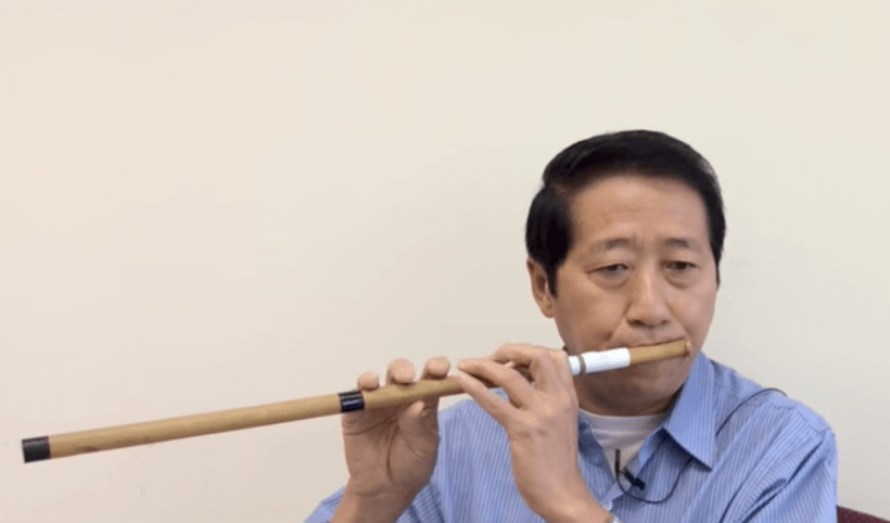 Asian man playing a wooden flute.