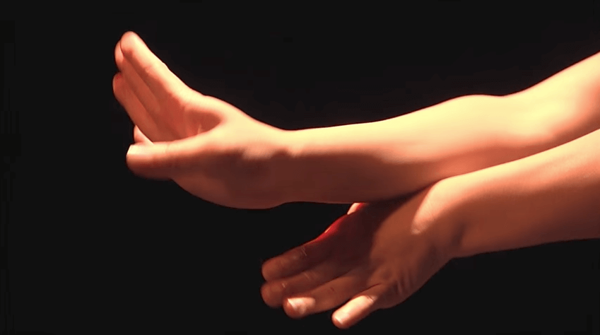 Hands in a dance pose in a dark studio.