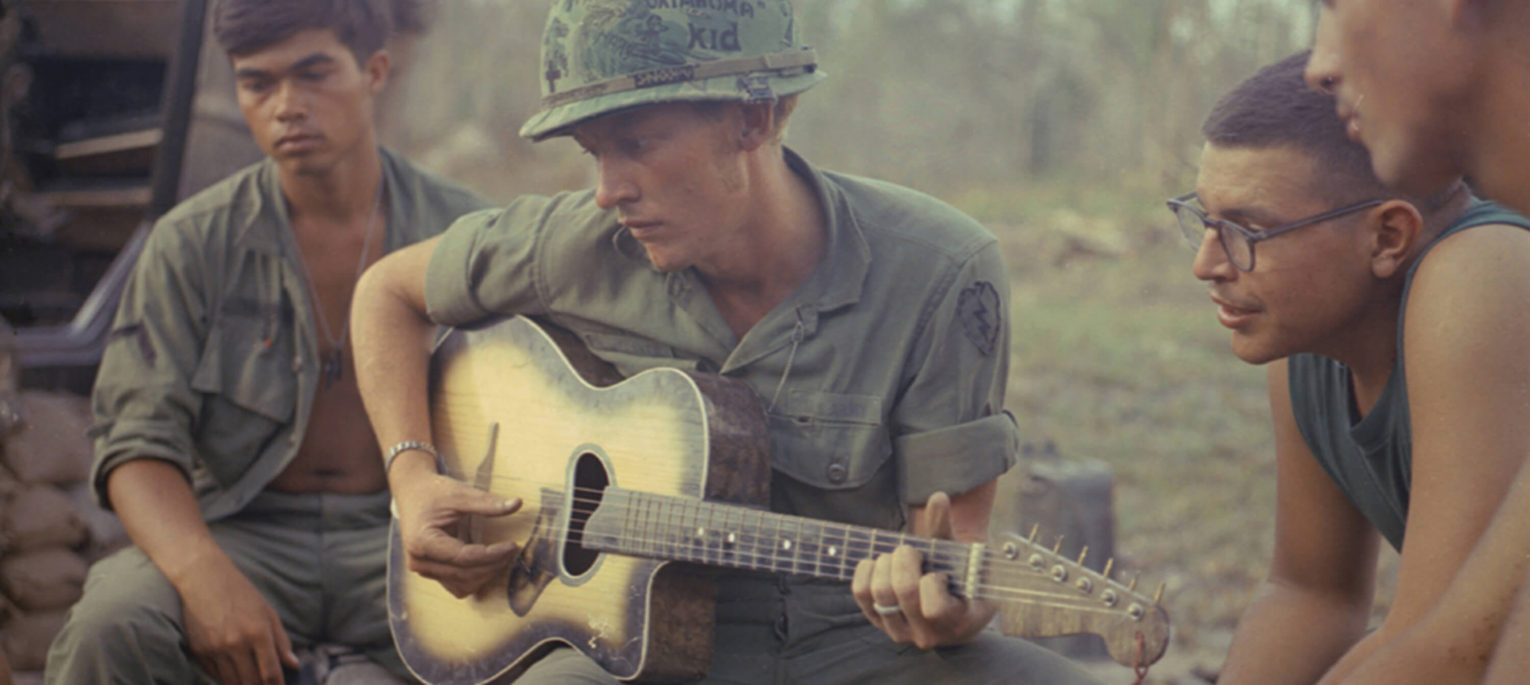 Vietnam soldiers listen to soldier playing guitar in camp.