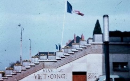 Graffiti on a building with a French flag flying atop it: "Vive le Viet-Cong!"