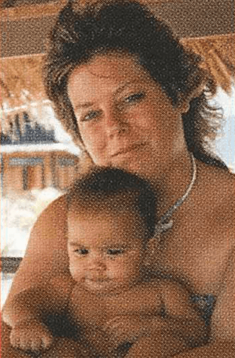 Photo of a woman outside, possibly a beach setting, with an infant sitting in her lap.