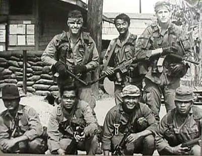 Two US and five Asian soldiers, posing for a photo in front of an encampment.