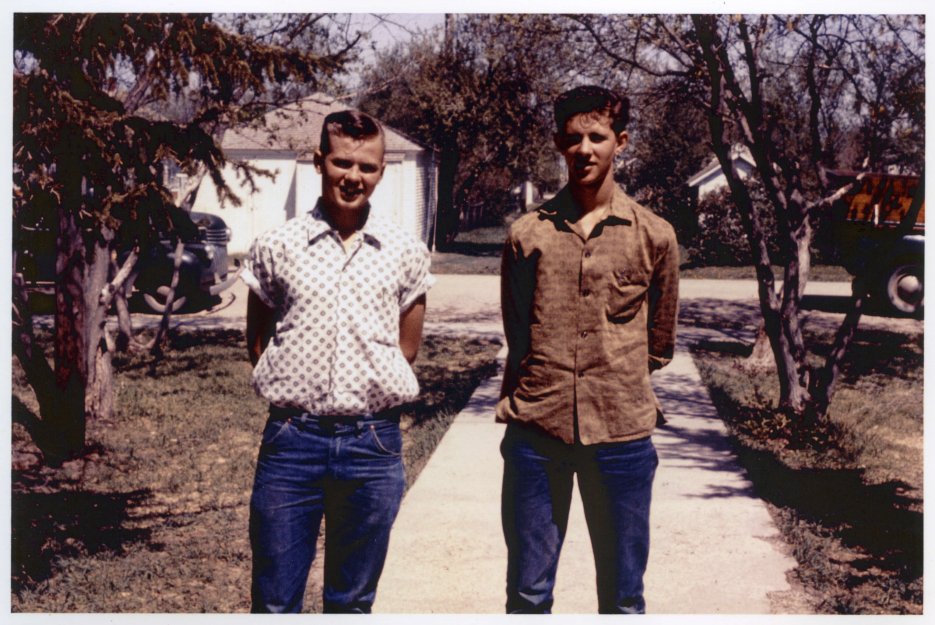 Two young men in civilian clothes, standing in a driveway in a residential area.