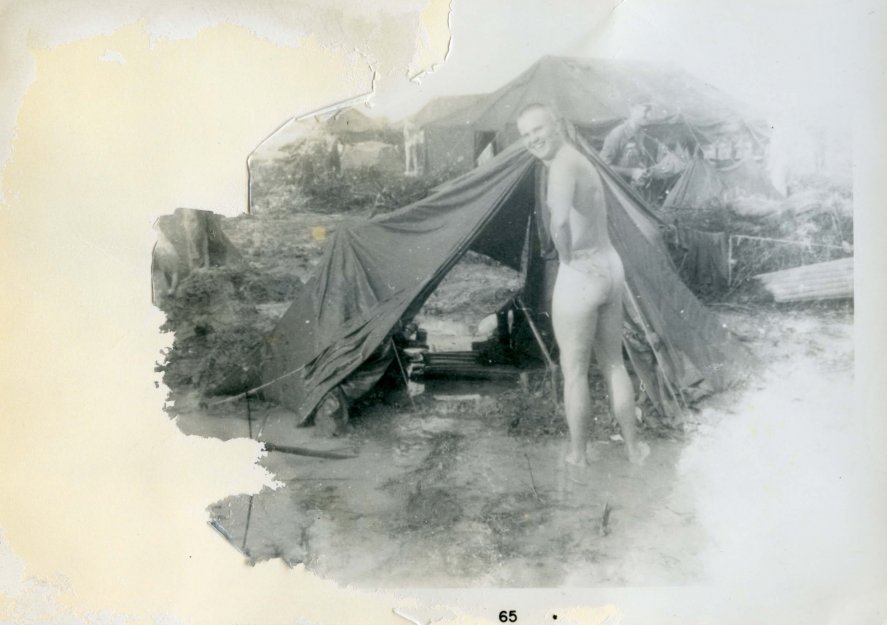 A tattered, torn, and faded photo of a young man, naked with his back to the camera, looking over his shoulder and laughing. Photo margins indicate the photo is from 1965.