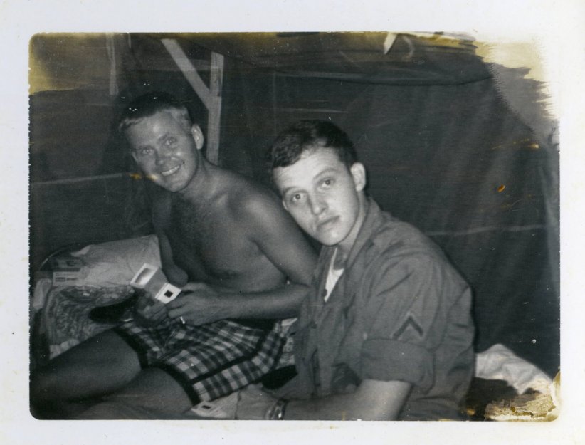 Aged photo of two young men sitting on a bunk in a barracks, looking at slides.
