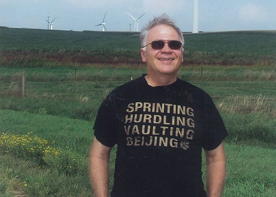Older gentleman, modern day, standing in front of a field with a wind turbine.