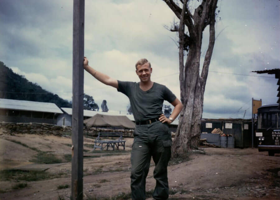 Young soldier leaning against a pole in an encampment.