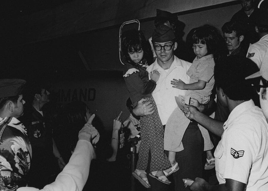 American soldier carrying two small Asian children, deplaning.