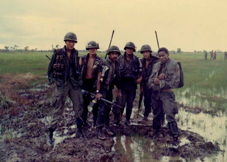 Six soldiers standing in muddy rice paddy fields.