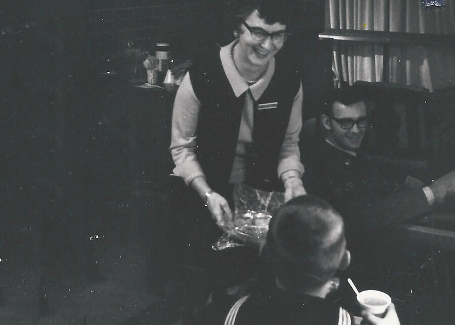 A woman with a drink tray serving a sailor, with a smile.