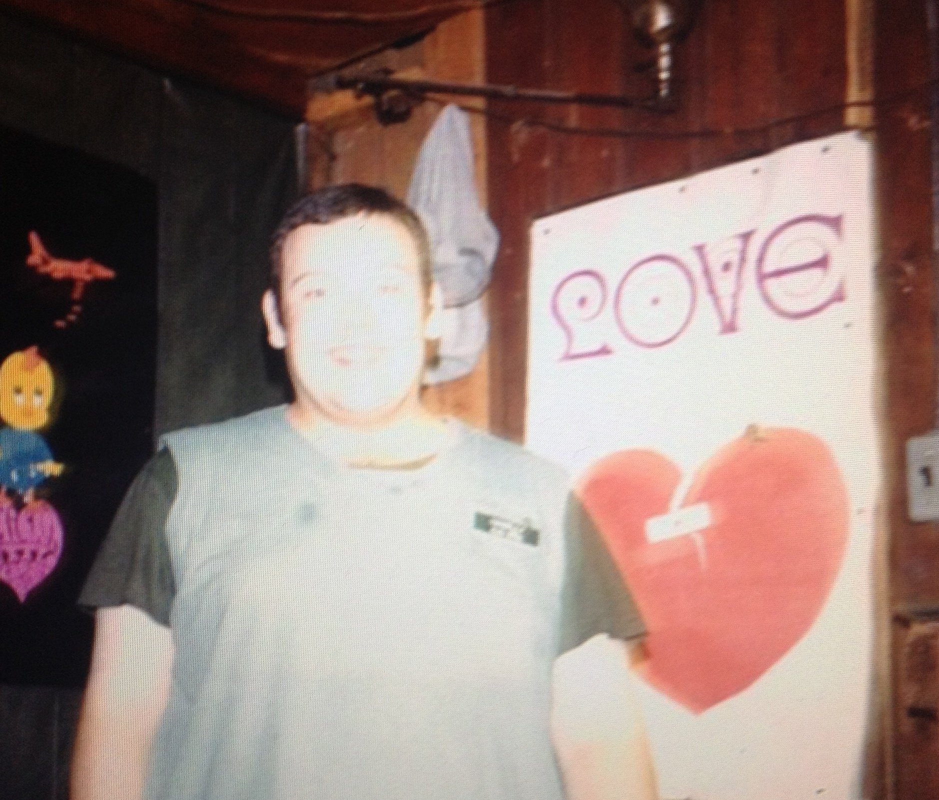 An overexposed photo of a large man in military scrubs standing in front of a poster that says "LOVE" and has a breaking heart on it.