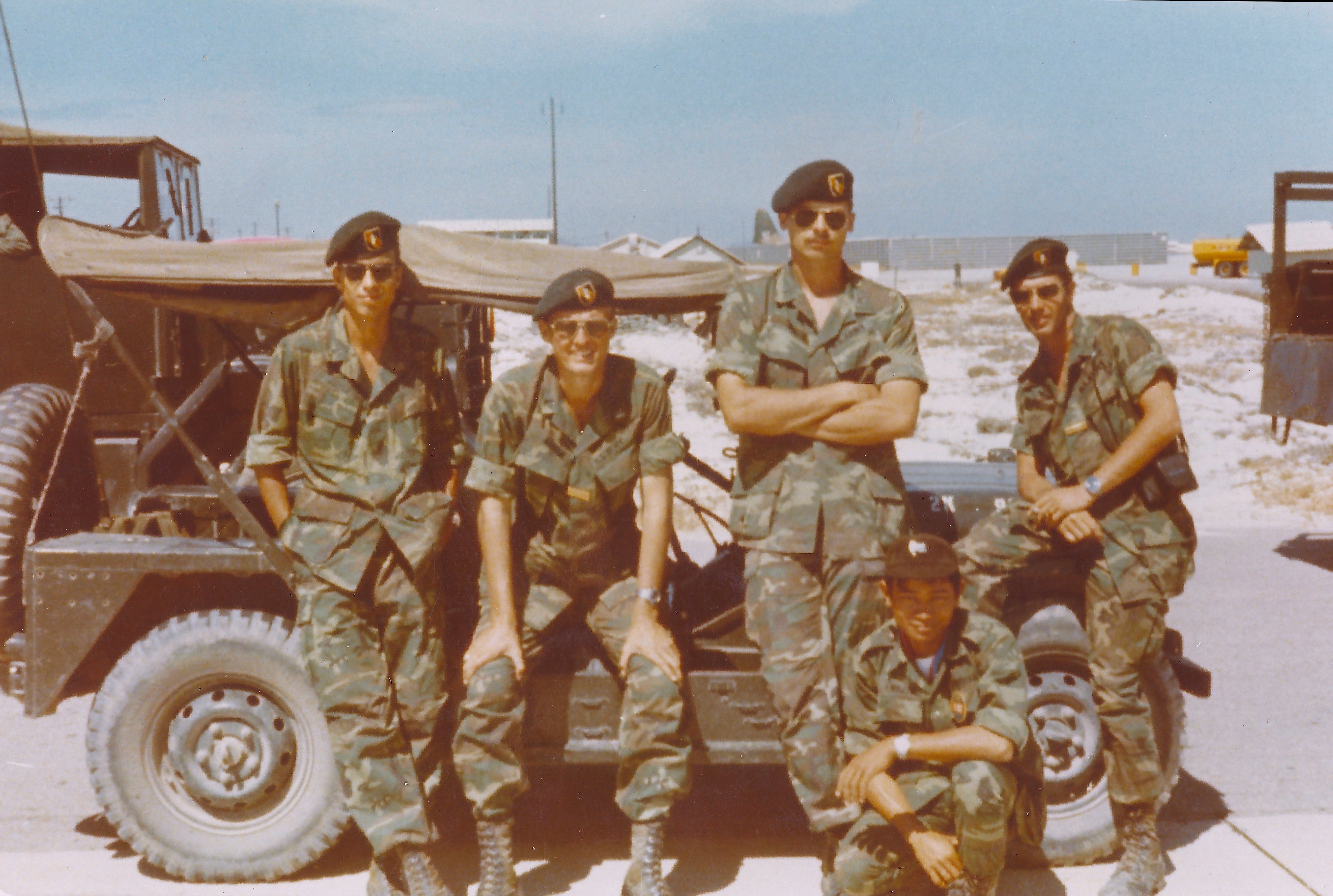 Four American soldiers leaning against a jeep with Cambodian soldier sitting on the ground.