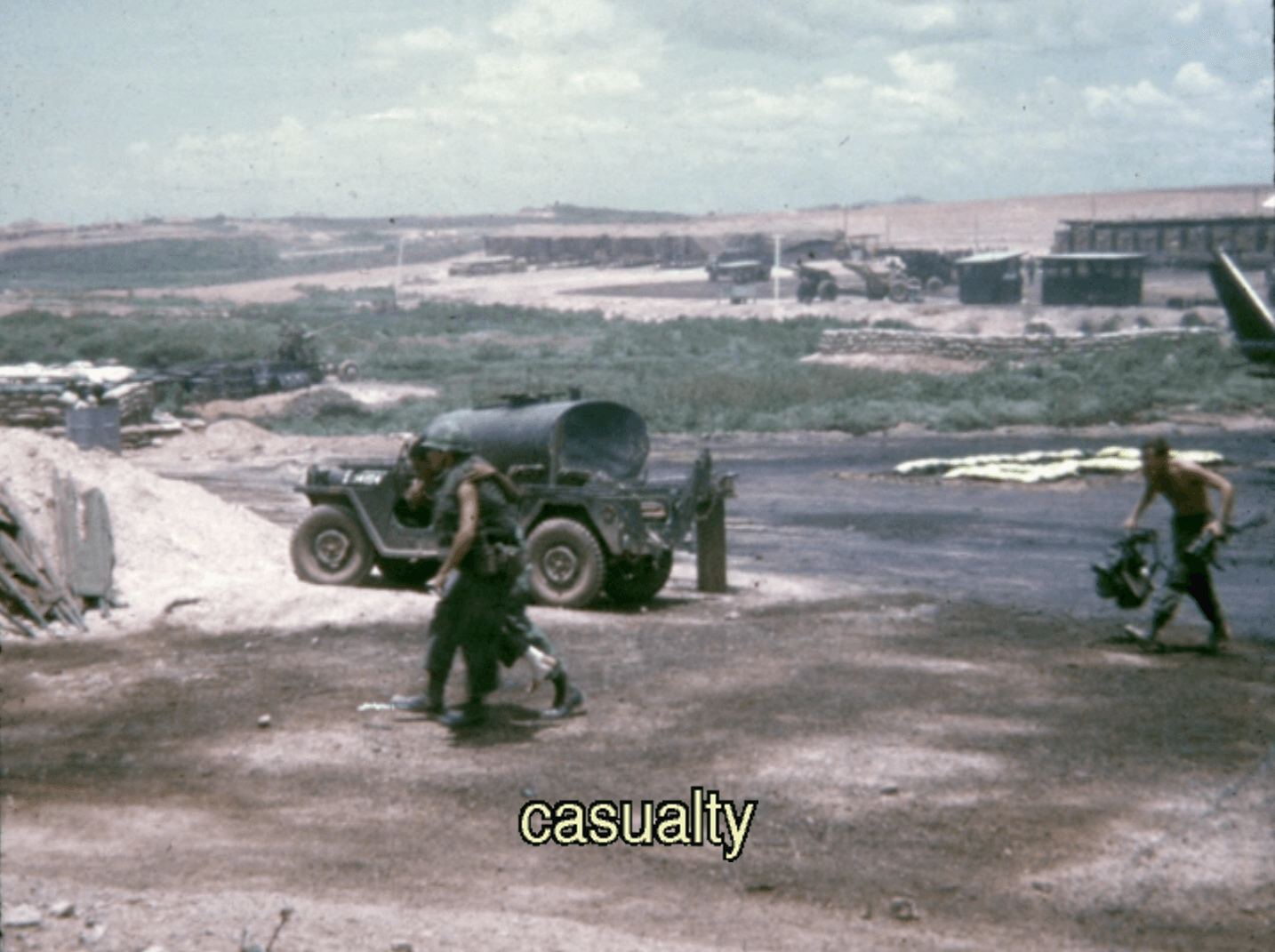 A soldier walking assisted with the help of another soldier; a third follows behind carrying gear. Text on photo says "casualty."