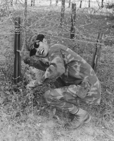 Cambodian soldier crouching by barbed wire fence.