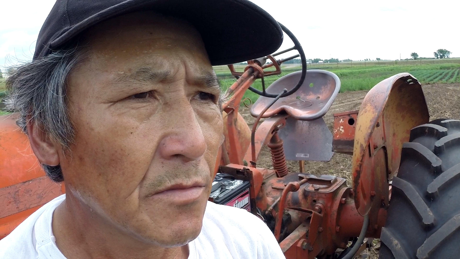 A stern-looking middle-aged Asian man standing next to farm equipment.