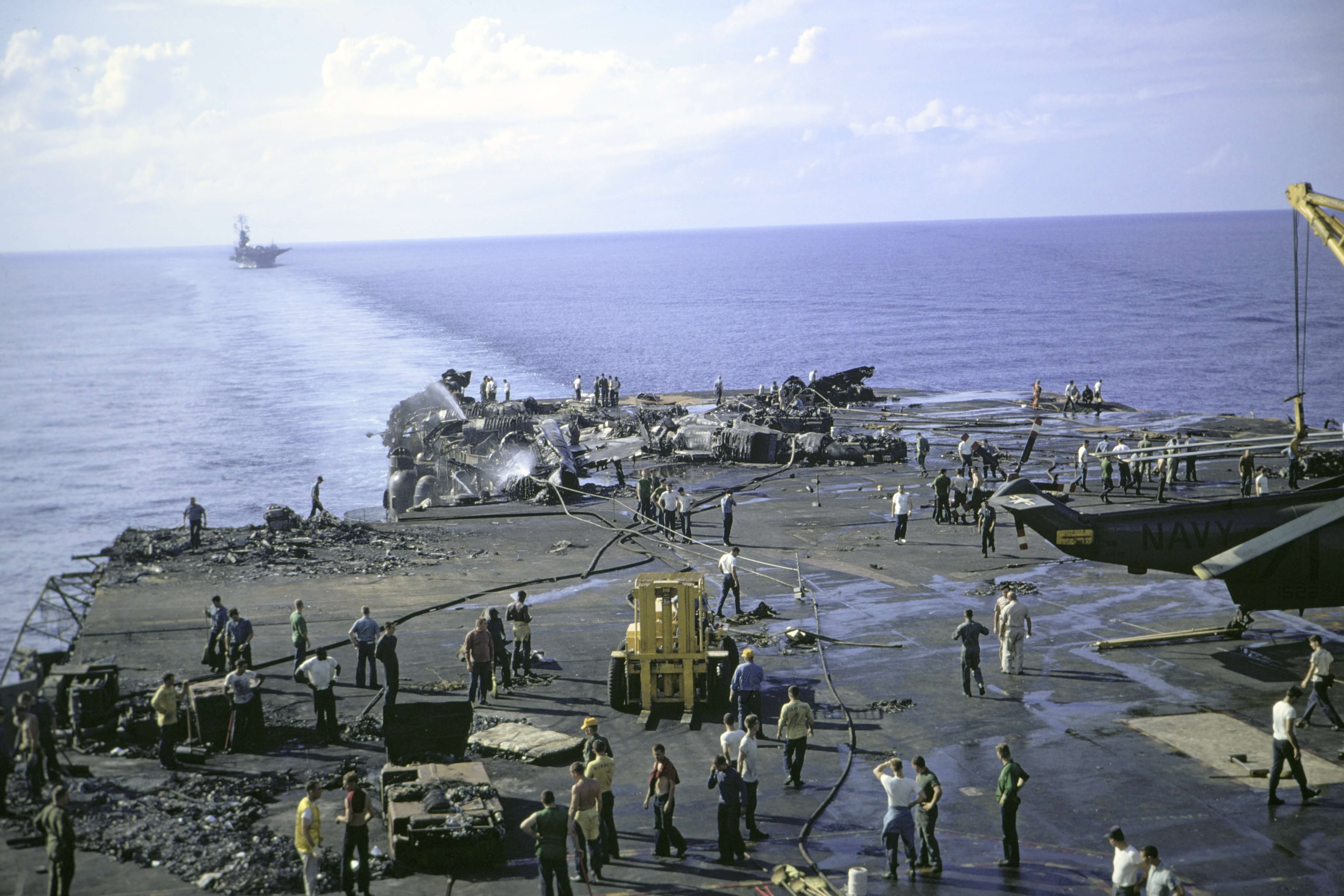 Wide shot of the deck of a large Navy boat, men standing and spraying down with fire hoses.